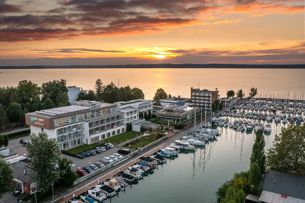 Légi felvétel a Hotel Yacht Siófokról naplementében, ahol a vitorláskikötő és a Balaton látható arany fényben