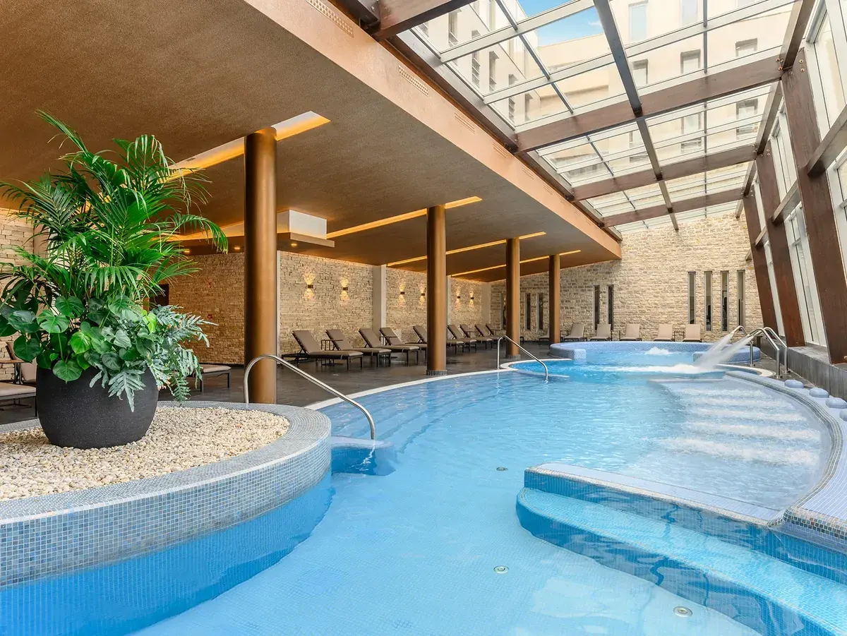 Wellness spa élménymedence üvegtetővel, napozóágyakkal és trópusi növényekkel
