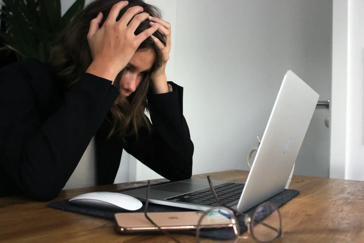 Stresszes nő laptop előtt, fejét fogva, munkahelyi kiégés és túlterheltség jelei